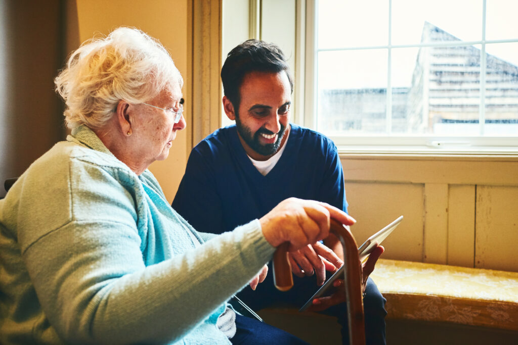 Nurse showing a digital tablet to an elderly woman in a care home.